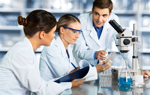 Three people in lab coats and goggles working with a microscope.