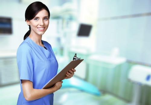 A woman in blue scrubs holding a clipboard.